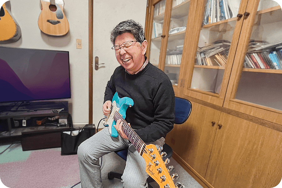 楽しそうに笑顔でギターを弾いている年配男性の写真